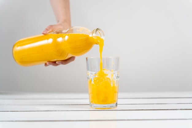 ガラスにオレンジジュースを注ぐクローズアップ手