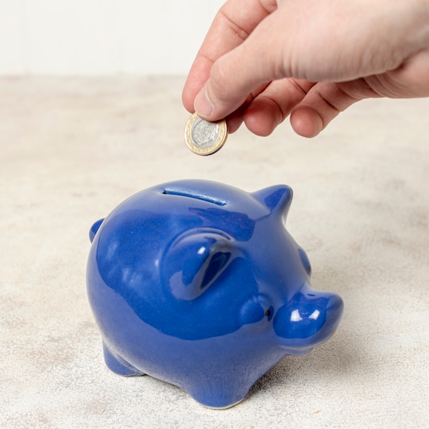 Close-up hand putting a coin in a piggy bank