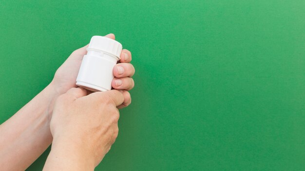 Close-up of hand's holding pill plastic bottle against green background