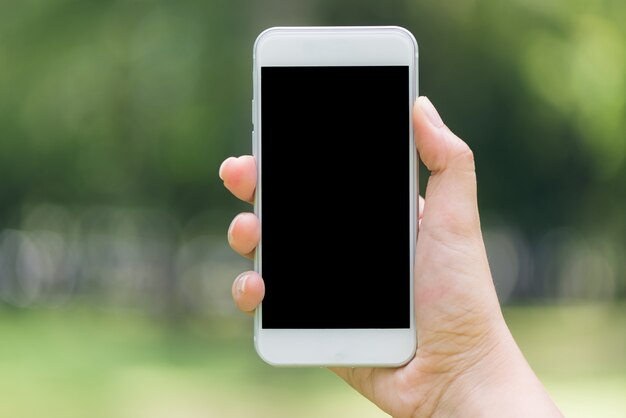 Крупным планом рука, показывая на телефоне мобильный пустой черный экран наружной концепции жизни на фоне размытой природы - можно использовать макет изображения. Винтажные картины стиля эффекта.