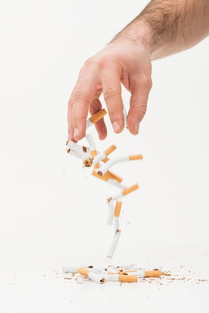 Close-up of hand throwing broken cigarettes against white background