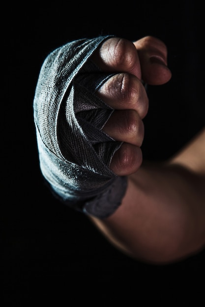Close-up hand with bandage of muscular man training kickboxing  on black