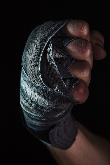 Foto gratuita mano del primo piano con la fasciatura del kickboxing di addestramento dell'uomo muscolare sul nero