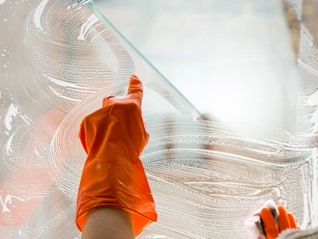 Close-up hand with rubber glove cleaning window