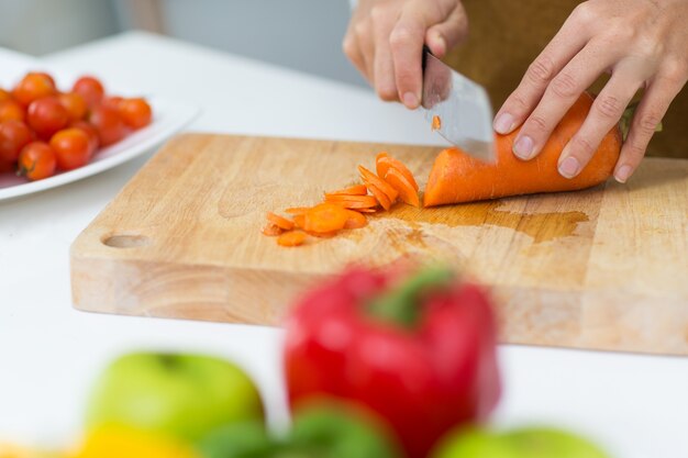 Close-up of hands chopping carrot on cutting board