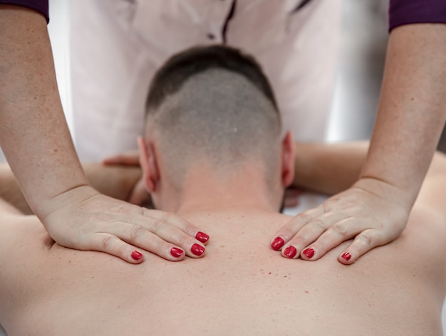 Free photo close-up of the hands of a female massage therapist in the process of kneading and massaging the male back.