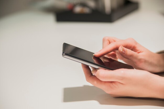 Close-up hands of the girl, sitting at the wooden table, in one hand is smartphone. Businesswoman surfing the Internet on smartphone.