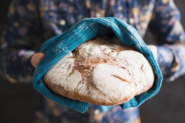 Крупным планом руки, держа испеченный хлеб, завернутый в синюю салфетку