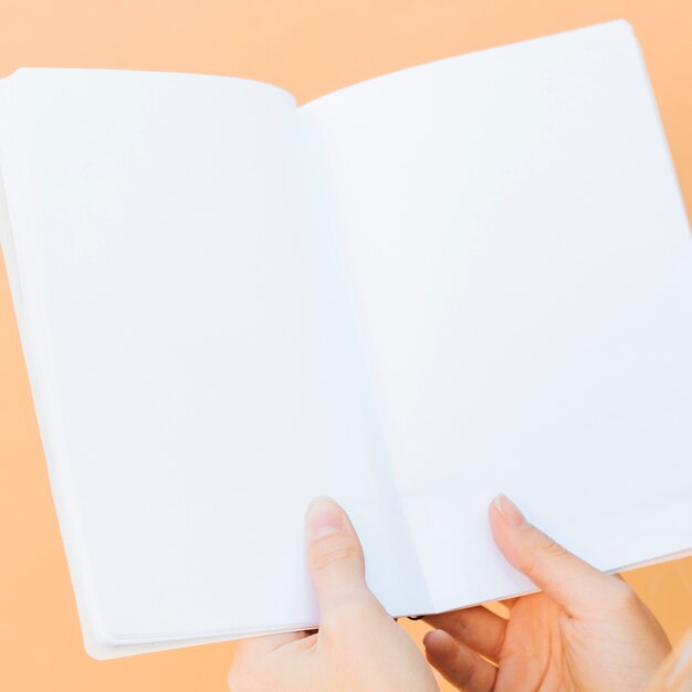 Close-up of hands holding blank white book against colored backdrop