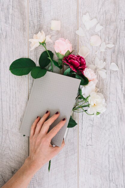 Close-up of hands holding diary with flowers on wooden table