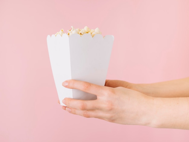 Foto gratuita mani del primo piano che tengono il contenitore di popcorn