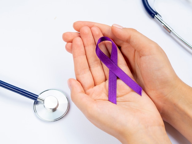 Close-up hands holding purple ribbon with stethoscope