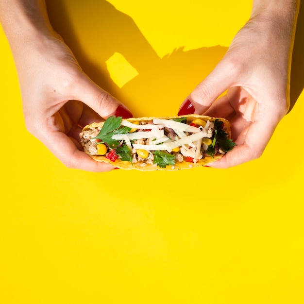 Close-up hands holding taco with yellow background