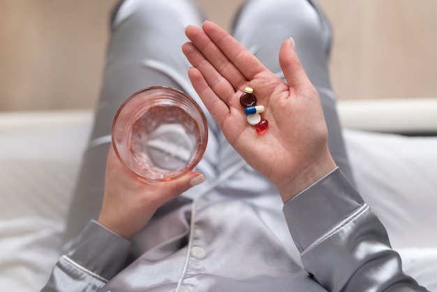 Foto gratuita chiuda sulle mani che tengono bicchiere d'acqua e pillole