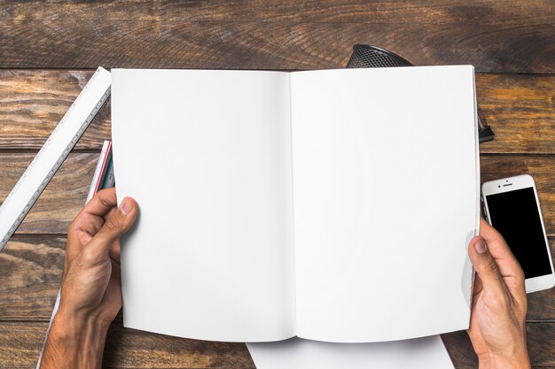 Close-up of hands holding white paper book over the wooden table