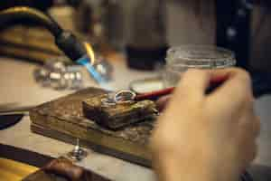 Free photo close up hands of jeweller, goldsmiths making of golden ring with gemstone using professional tools