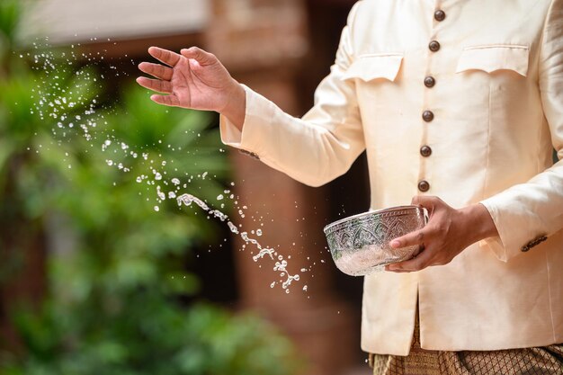 4月のソンクラン祭りタイ新年家族の日に寺院で水入れで水しぶきをはねかける美しいタイの衣装で男の手をクローズアップ