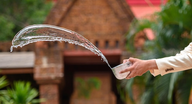 4月のソンクラン祭りタイ新年家族の日に寺院で水入れで水しぶきをはねかける美しいタイの衣装で男の手をクローズアップ