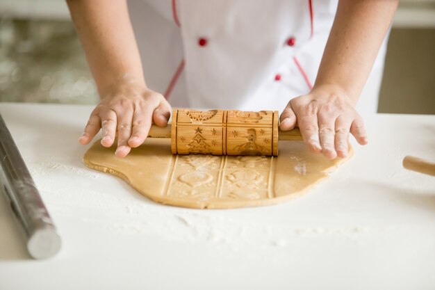 Close up of hands rolling gingerbread dough with patterned rolle