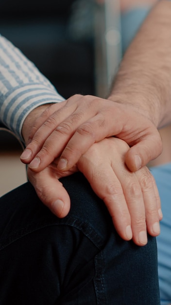 Close up of hands of senior patient and medical assistant at nursing facility. Nurse giving assistance to person sitting in wheelchair. Healthcare specialist showing support to disabled adult