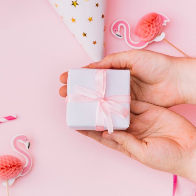 Close-up of hands showing white wrapped gift box tied with pink ribbon