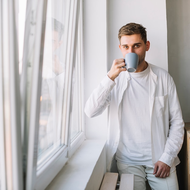 Free photo close-up of a handsome guy drinking beverage standing near window