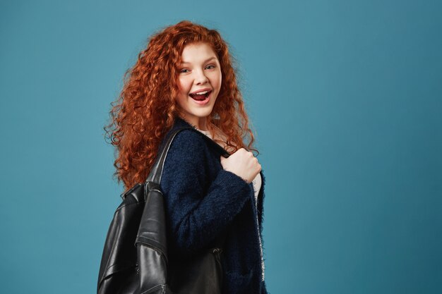 Close up of handsome happy ginger student woman with wavy hair holding backpack with hand, happily smiling.