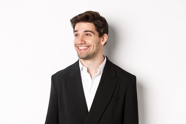 Close-up of handsome male entrepreneur in suit, looking left and smiling, standing against white background.