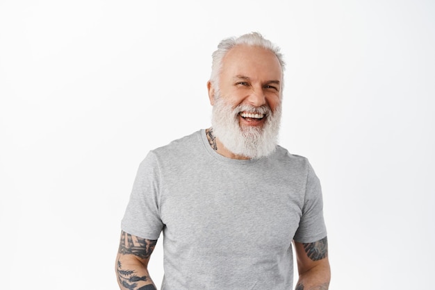 Free photo close up of handsome senior man with tattoos and beard laughing and looking candid aside chatting and having fun standing happy against white background