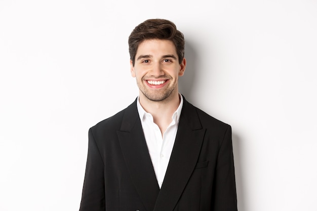 Close-up of handsome young businessman in trendy suit smiling, standing against white background