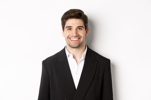 Close-up of handsome young businessman in trendy suit smiling, standing against white background