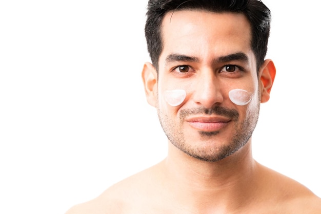 Close-up of a handsome young male with moisturizer cream on cheeks in studio