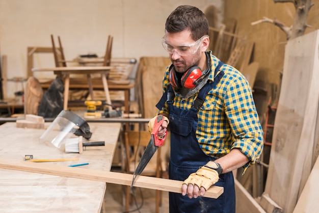 Close-up of a handyman sawing long wooden plank