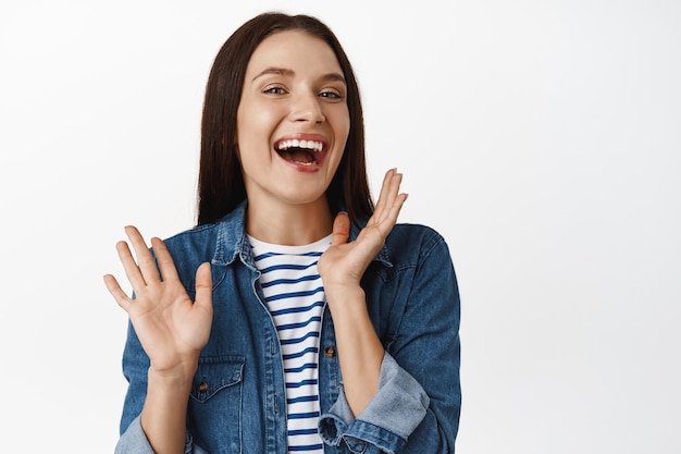 Close up of happy adult brunette woman laughing, enjoy conversation, shaking hands and gesturing casually, smiling and giggling, standing against white background.