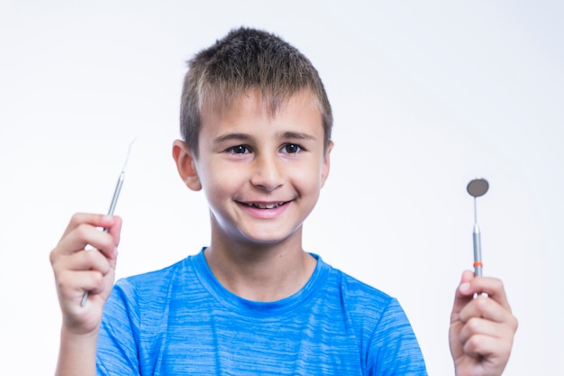 Close-up of a happy boy holding dental mirror and scaler on white background