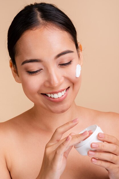 Close-up happy brunette woman with face cream 