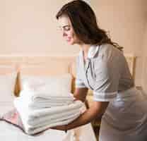 Free photo close-up of happy chambermaid putting stack of fresh white bath towels on the bed