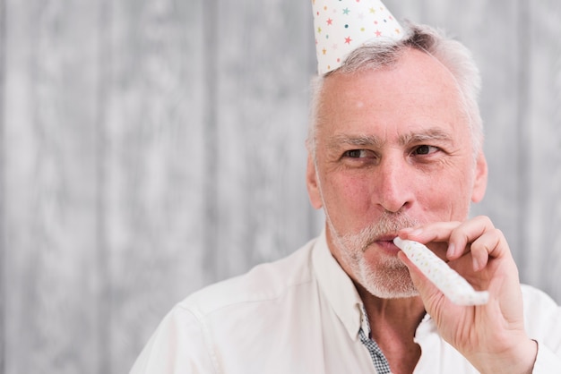 Close-up of a happy elder man blowing party blower