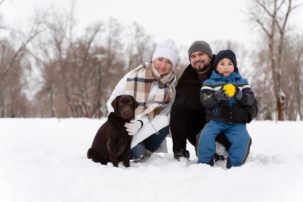 Крупным планом счастливая семья, играющая в снегу с собакой