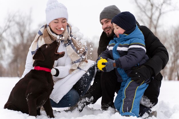 Крупным планом счастливая семья, играющая в снегу с собакой