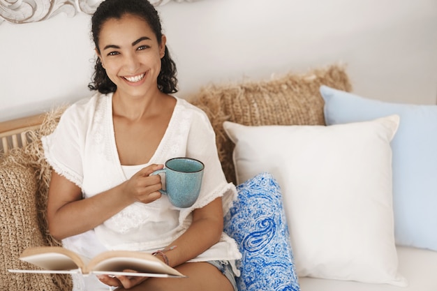 Close-up happy healthy young woman with dark curly hair lying in comfortable sofa in a terrace