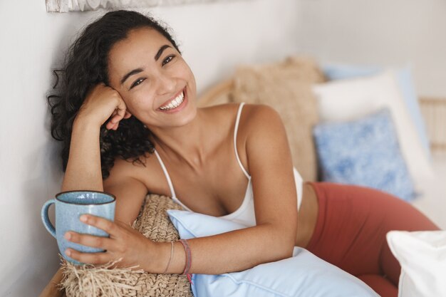 Close-up happy healthy young woman with dark curly hair lying in comfortable sofa in a terrace