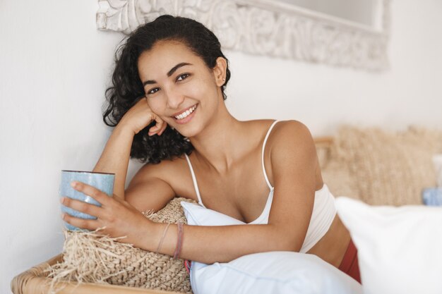 Close-up happy healthy young woman with dark curly hair lying in comfortable sofa in a terrace