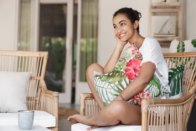 Close-up happy healthy young woman with dark curly hair sitting in comfortable sofa in a terrace