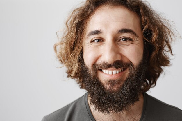 Close-up of happy middle-eastern man with long beard and curly haircut smiling joyful