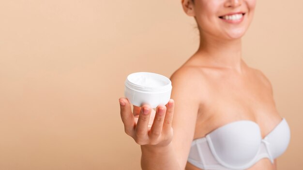 Close-up happy model with cream jar and white bra