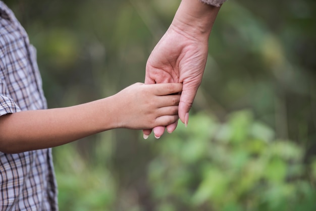 Close up of happy mum and son holding hand in a park. Family concept.