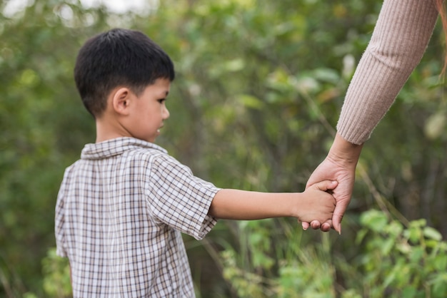 Close up of happy mum and son holding hand in a park. Family concept.