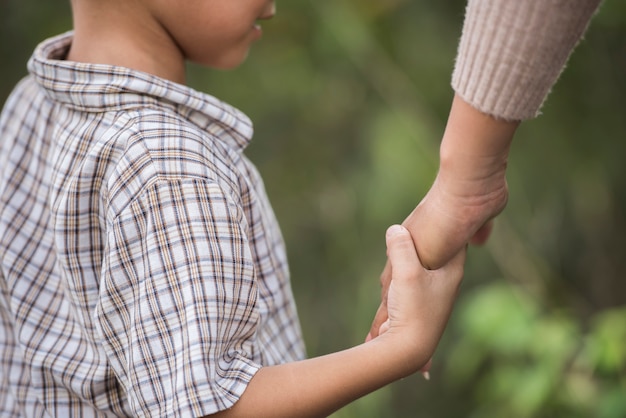 Close up of happy mum and son holding hand in a park. Family concept.