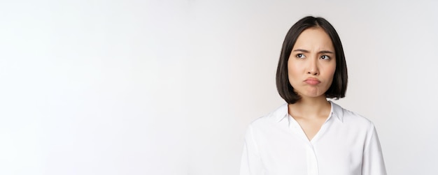 Close up head portrait of young asian woman looking upset and disappointed at left copy space grimac